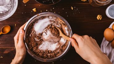 tigela com ingredientes vista de cima. A imagem mostra as mãos de uma pessoa. Uma segura a tigela e a outra mistura os ingredientes com uma colher de madeira.